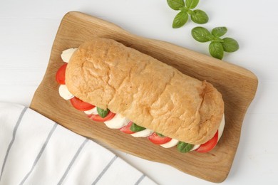 Photo of Tasty sandwich with mozzarella cheese, tomatoes and basil on white wooden table, flat lay