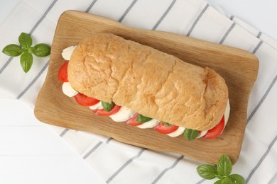 Photo of Tasty sandwich with mozzarella cheese, tomatoes and basil on white table, top view