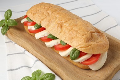 Photo of Tasty sandwich with mozzarella cheese, tomatoes and basil on white table, closeup