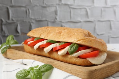 Photo of Tasty sandwich with mozzarella cheese, tomatoes and basil on table against grey textured wall, closeup