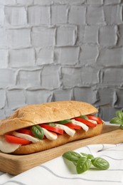 Photo of Tasty sandwich with mozzarella cheese, tomatoes and basil on table against grey textured wall, closeup. Space for text