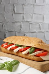 Photo of Tasty sandwich with mozzarella cheese, tomatoes and basil on table against grey textured wall, closeup. Space for text