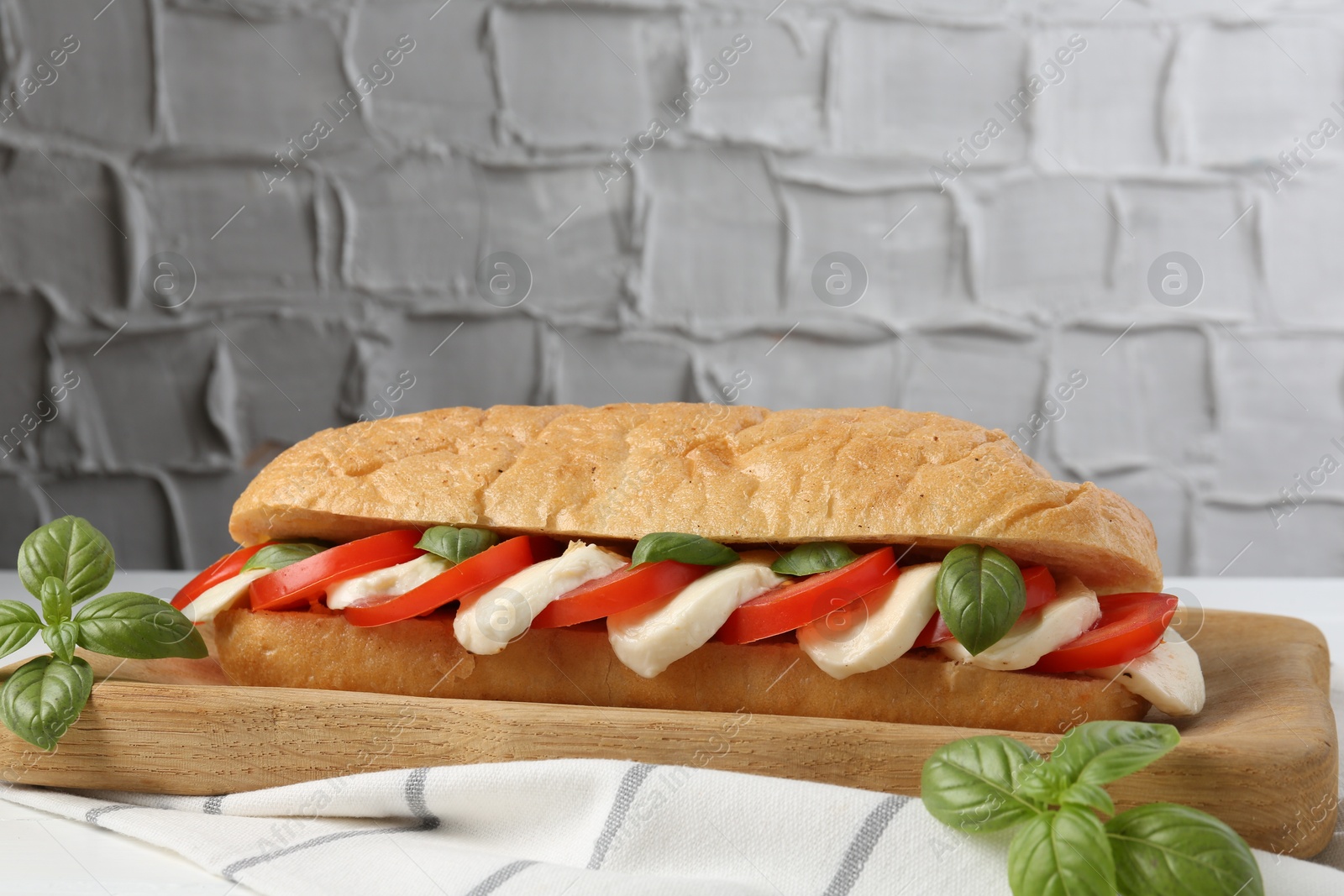 Tasty sandwich with mozzarella cheese, tomatoes and basil on white table against grey textured wall, closeup. Space for text Photo of Tasty sandwich with mozzarella cheese, tomatoes and basil on white table against grey textured wall, closeup. Space for text