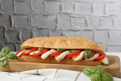 Photo of Tasty sandwich with mozzarella cheese, tomatoes and basil on white table against grey textured wall, closeup. Space for text