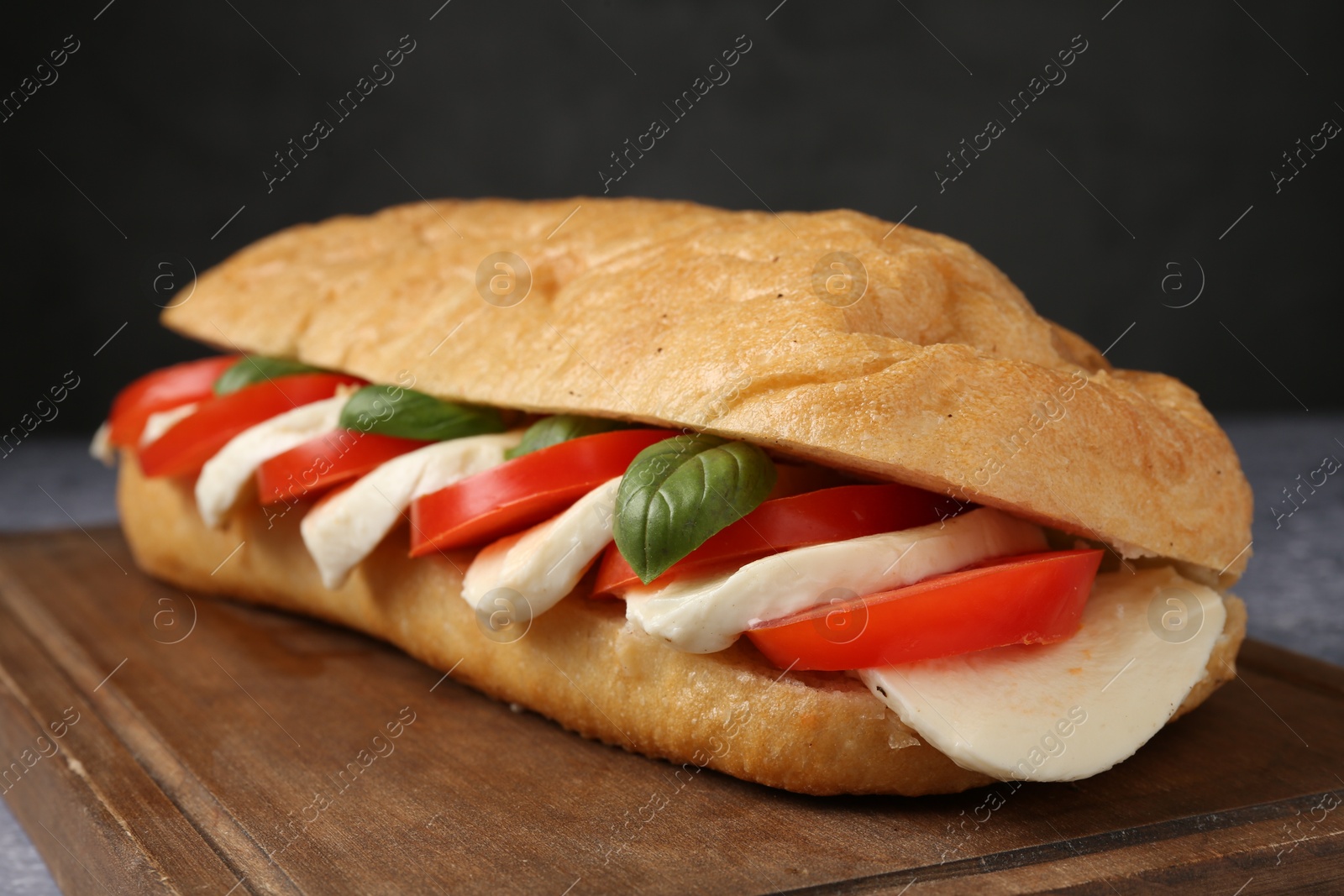 Tasty sandwich with mozzarella cheese, tomatoes and basil on grey table against black background, closeup Photo of Tasty sandwich with mozzarella cheese, tomatoes and basil on grey table against black background, closeup