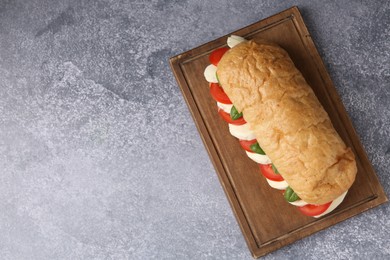 Photo of Tasty sandwich with mozzarella cheese, tomatoes and basil on grey textured table, top view. Space for text
