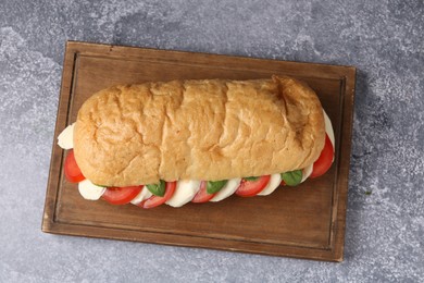 Photo of Tasty sandwich with mozzarella cheese, tomatoes and basil on grey textured table, top view