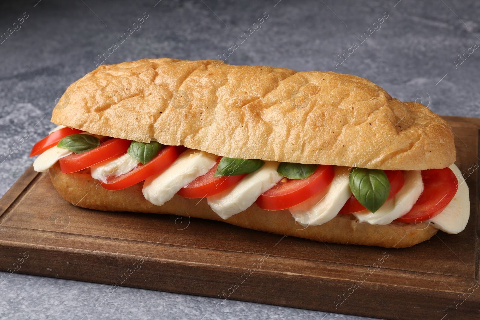 Tasty sandwich with mozzarella cheese, tomatoes and basil on grey textured table, closeup Photo of Tasty sandwich with mozzarella cheese, tomatoes and basil on grey textured table, closeup