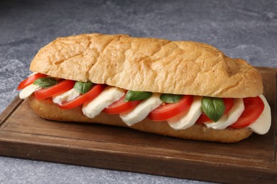 Photo of Tasty sandwich with mozzarella cheese, tomatoes and basil on grey textured table, closeup