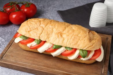 Photo of Tasty sandwich with mozzarella cheese, tomatoes and basil on grey textured table, closeup