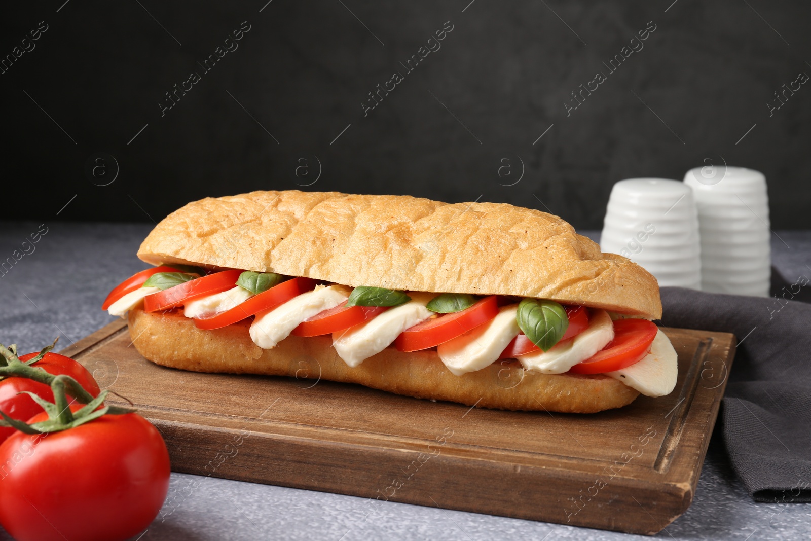 Tasty sandwich with mozzarella cheese, tomatoes and basil on grey textured table against dark background, closeup Photo of Tasty sandwich with mozzarella cheese, tomatoes and basil on grey textured table against dark background, closeup