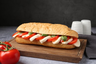 Photo of Tasty sandwich with mozzarella cheese, tomatoes and basil on grey textured table against dark background, closeup