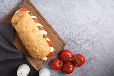 Photo of Tasty sandwich with mozzarella cheese, tomatoes and basil on grey textured table, flat lay. Space for text