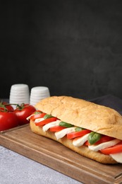 Photo of Tasty sandwich with mozzarella cheese, tomatoes and basil on grey textured table against dark background, closeup. Space for text