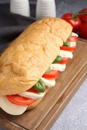 Photo of Tasty sandwich with mozzarella cheese, tomatoes and basil on grey textured table, closeup