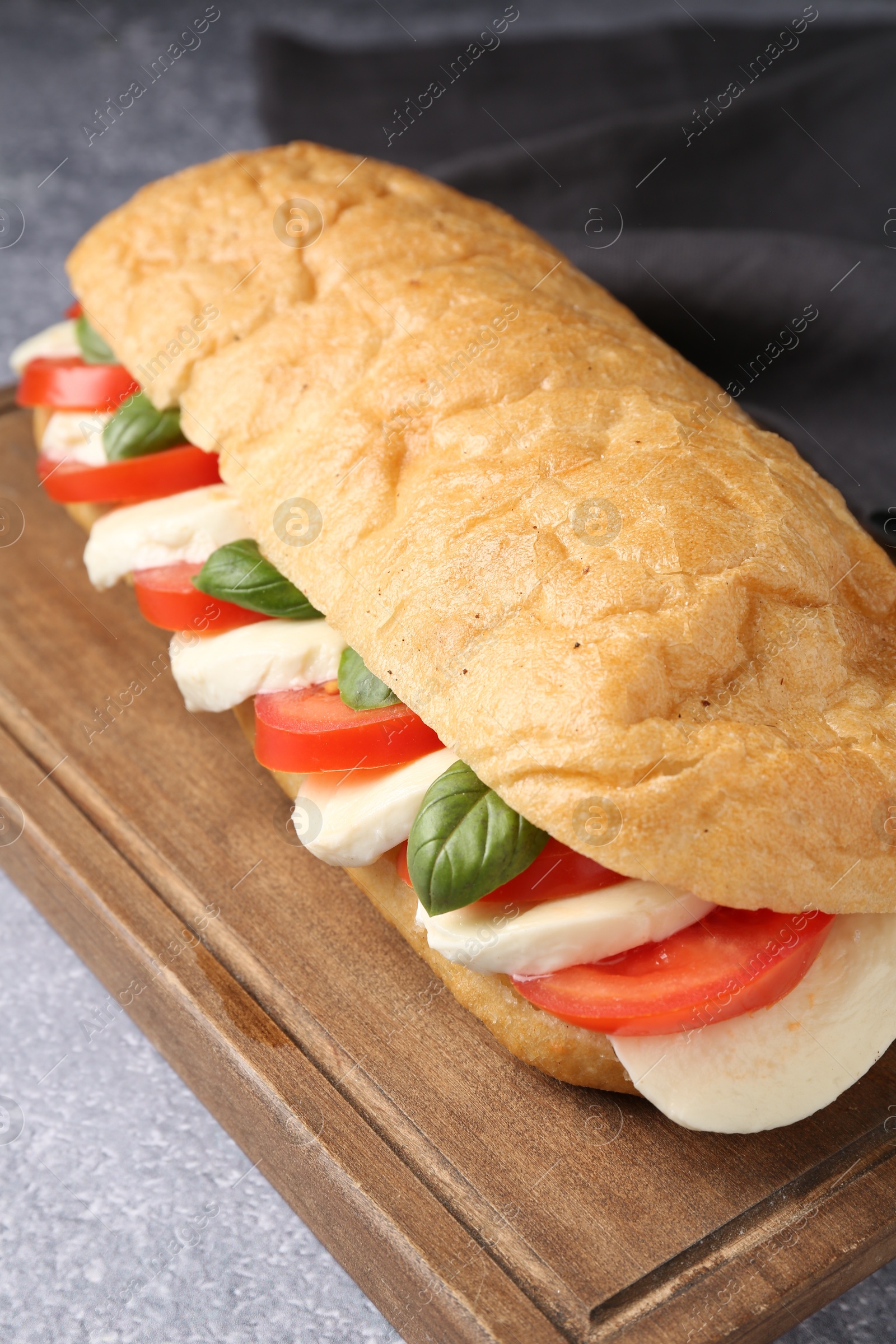 Tasty sandwich with mozzarella cheese, tomatoes and basil on grey textured table, closeup Photo of Tasty sandwich with mozzarella cheese, tomatoes and basil on grey textured table, closeup