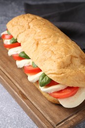Photo of Tasty sandwich with mozzarella cheese, tomatoes and basil on grey textured table, closeup
