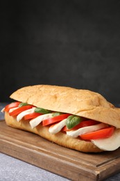 Photo of Tasty sandwich with mozzarella cheese, tomatoes and basil on grey textured table against dark background, closeup