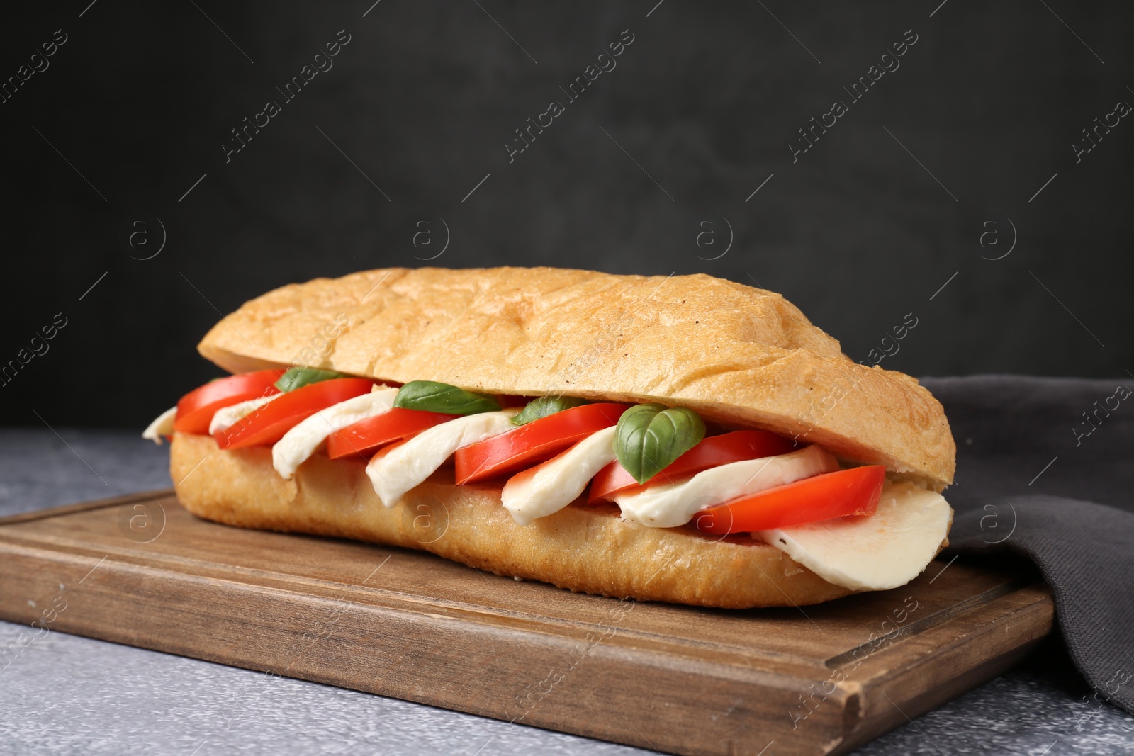 Tasty sandwich with mozzarella cheese, tomatoes and basil on grey textured table against dark background, closeup Photo of Tasty sandwich with mozzarella cheese, tomatoes and basil on grey textured table against dark background, closeup