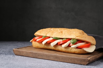 Photo of Tasty sandwich with mozzarella cheese, tomatoes and basil on grey textured table against dark background, closeup