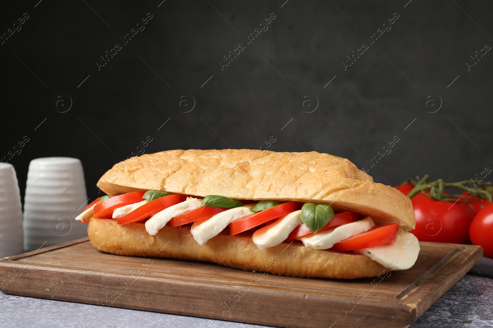 Tasty sandwich with mozzarella cheese, tomatoes and basil on grey textured table against dark background, closeup Photo of Tasty sandwich with mozzarella cheese, tomatoes and basil on grey textured table against dark background, closeup
