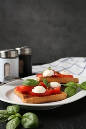 Photo of Tasty sandwiches with mozzarella cheese, tomatoes and basil on dark textured table against grey background, closeup