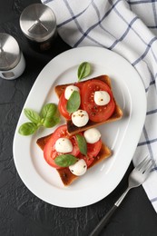 Photo of Tasty sandwiches with mozzarella cheese, tomatoes, basil and fork on dark textured table, flat lay