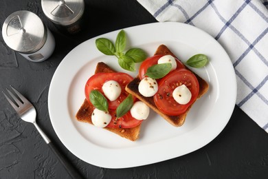 Photo of Tasty sandwiches with mozzarella cheese, tomatoes, basil and fork on dark textured table, flat lay