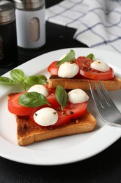 Photo of Tasty sandwiches with mozzarella cheese, tomatoes, basil and fork on black table, closeup