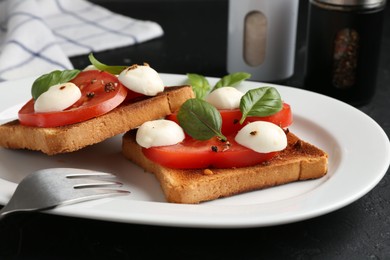 Photo of Tasty sandwiches with mozzarella cheese, tomatoes, basil and fork on dark textured table, closeup