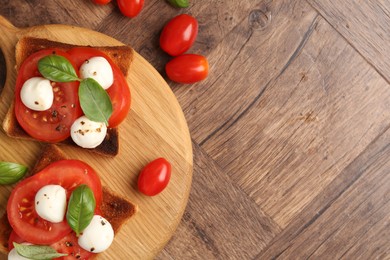 Photo of Tasty sandwiches with mozzarella cheese, tomatoes and basil on wooden table, flat lay. Space for text