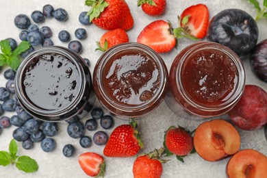 Photo of Different sweet jams in jars and ingredients on grey table, flat lay