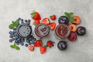 Photo of Different sweet jams in jars and ingredients on grey table, flat lay