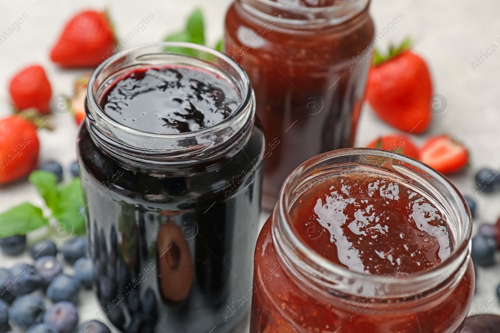 Different sweet jams in jars and ingredients on table, closeup Photo of Different sweet jams in jars and ingredients on table, closeup