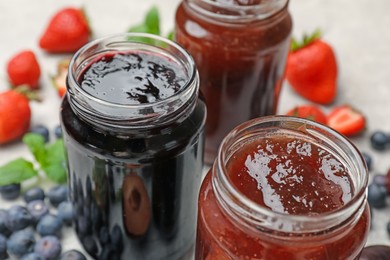 Photo of Different sweet jams in jars and ingredients on table, closeup