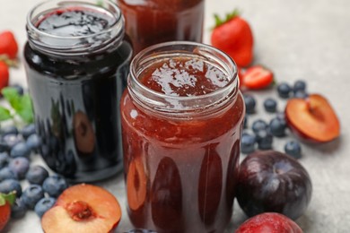 Photo of Different sweet jams in jars and ingredients on grey table, closeup