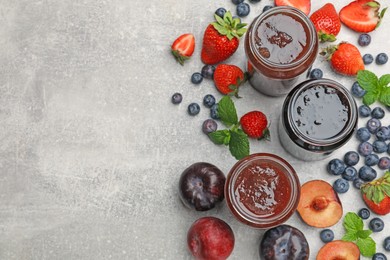 Photo of Different sweet jams in jars and ingredients on grey table, flat lay. Space for text