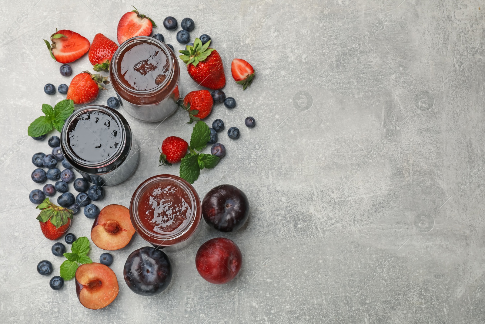 Different sweet jams in jars and ingredients on grey table, flat lay. Space for text Photo of Different sweet jams in jars and ingredients on grey table, flat lay. Space for text