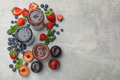 Photo of Different sweet jams in jars and ingredients on grey table, flat lay. Space for text