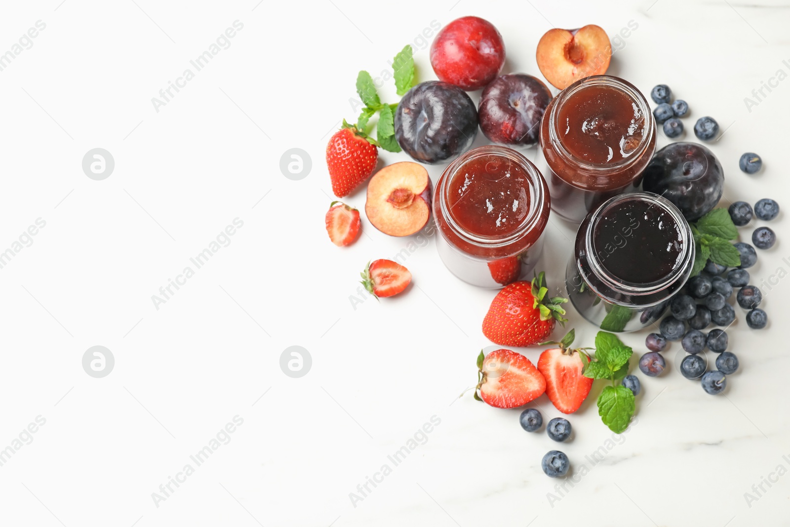 Different sweet jams in jars and ingredients on white marble table, flat lay. Space for text Photo of Different sweet jams in jars and ingredients on white marble table, flat lay. Space for text