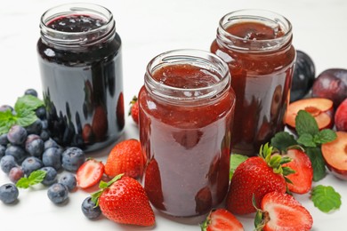 Photo of Different sweet jams in jars and ingredients on white table, closeup