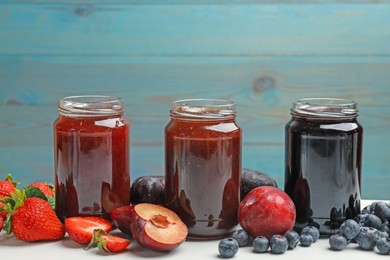 Photo of Different sweet jams in jars and ingredients on white table