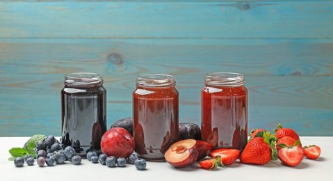Photo of Different sweet jams in jars and ingredients on white table