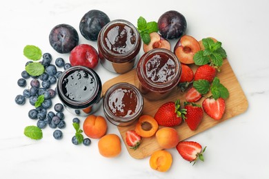 Photo of Different sweet jams in jars and ingredients on white marble table, flat lay