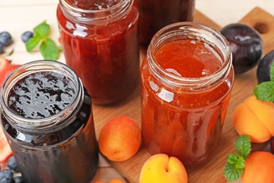 Photo of Tasty sweet jams in jars and ingredients on light table, closeup