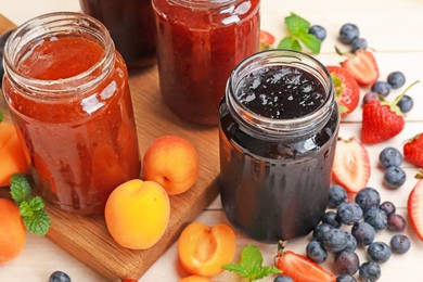 Photo of Tasty sweet jams in jars and ingredients on light wooden table, closeup