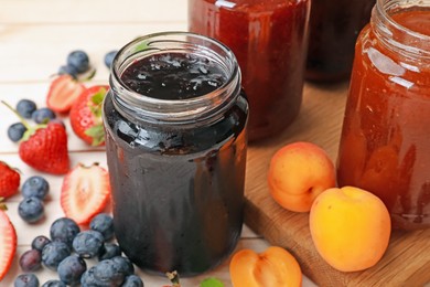 Photo of Tasty sweet jams in jars and ingredients on light wooden table, closeup