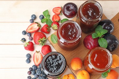 Photo of Tasty sweet jams in jars surrounded by ingredients on light wooden table, flat lay