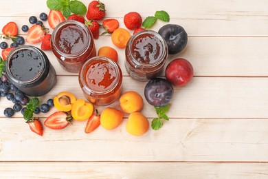 Photo of Tasty sweet jams in jars surrounded by ingredients on light wooden table, flat lay. Space for text