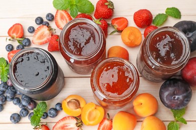 Photo of Tasty sweet jams in jars surrounded by ingredients on light wooden table, flat lay